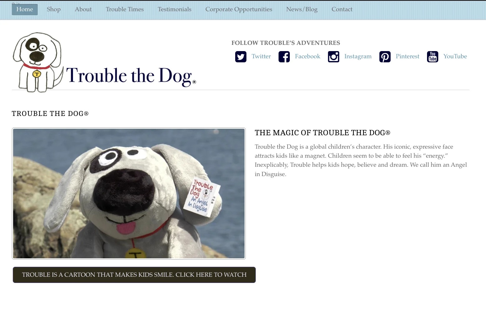 The earlier Trouble the Dog homepage: a pale blue menu bar, the logo beside a row of social media links, a photo of the plush dog on a rock, a short paragraph, and a dark button that says Trouble is a cartoon that makes kids smile. There is no way to buy above the fold.